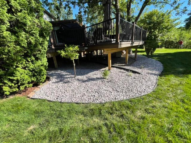 Gray stone landscaping beneath a raised backyard deck, edged neatly against the surrounding lawn.