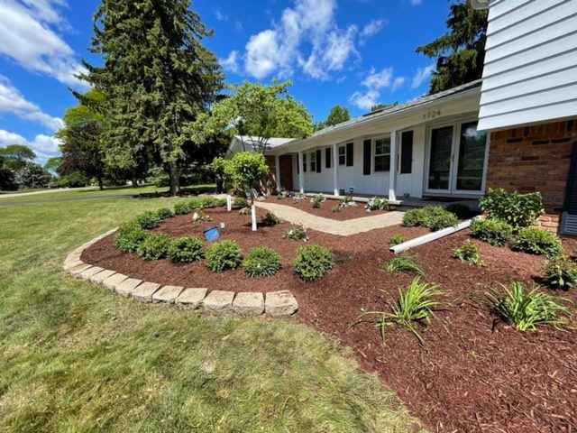 Front-yard landscape with stone-edged mulch beds, boxwood shrubs, and a paver walkway.
